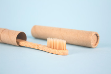 Close up of natural bamboo toothbrushe packed in reusable paper tube on blue background with copy space. Sustainable lifestyle and plastic free concept, bathroom essentials in zero waste home, mockup
