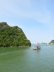 Boats on a cruise in Halong Bay, Vietnam. Rocks in the background and blue sky.