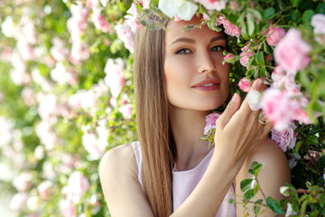 Fototapeta premium Beautiful young woman in nature in roses. Brunette girl with roses.