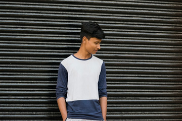 a teenager guy portrait looking down in front of a metal gate wearing white t-shirt with space for...