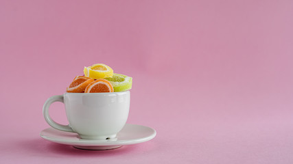 Colourful fruit Jelly candy in a white coffee cup against pink background for food and snack concept