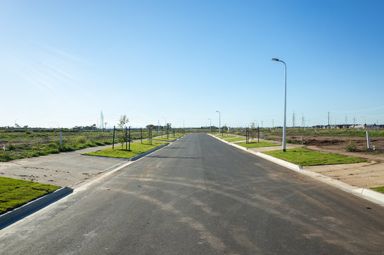 Asphalt road between vacant lands in a new residential suburb. Tarneit, Melbourne, VIC Australia. Concept of real estate development, housing, urbanization, and land for sale.