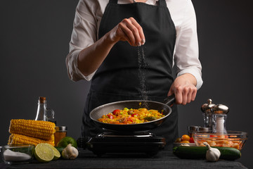 Frying vegetables, the chef salts in the freeze in motion. Against the background of vegetables. Delicious and wholesome food