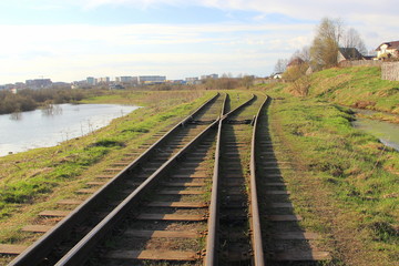 Fototapeta premium The railway stretching into the distance against the background of young green grass and trees in spring.