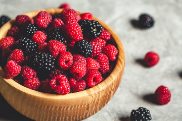 raspberries and blackberries in wood bowl on gray table, vintage