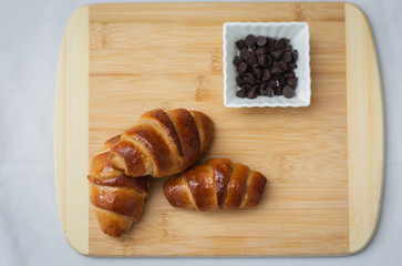 homemade whole spelled flour croissants, on a wooden surface, next to chocolate chips in a small ceramic square bowl,