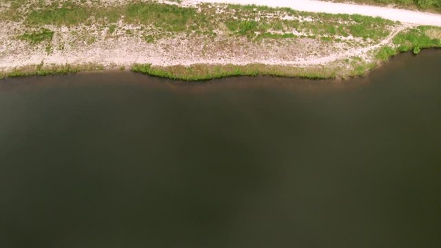 Drone flight from a lake to forrest with small stream and dirt road, top view