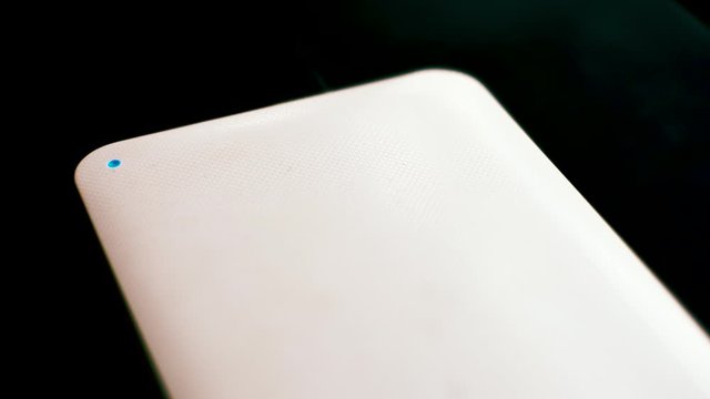 White mobile external hard drive on black background with blinking blue LED indicator light diode while writing on the disk