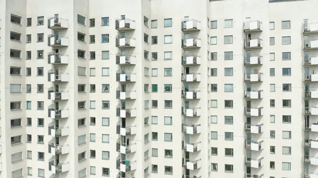Exterior of a high rise multi story residential apartment building - white facade, windows & balconies. Establishing shot rising ascending aerial footage.