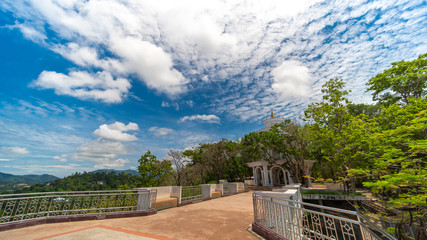 Terrace and stanless fence with cement chair at viewpoint on hilltop with green leaves tree. Beautiful white cloud sky background. Nature and travel concept