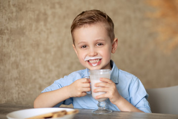 An adorable European baby drinks milk from a glass cup. The boy loves dairy products. The child is...