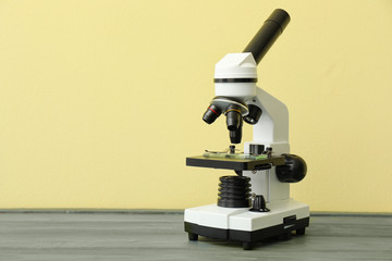 Modern microscope on table against color background