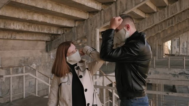 Close-up of guy and girl in protective medical masks hitting their elbows instead of shaking hands. Pandemic panic and new ways of contact during quarantine. Safe way to bump elbows instead handshake.