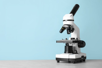 Modern microscope on table against color background