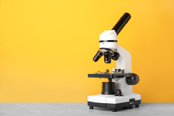 Modern microscope on table against color background