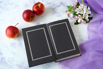 unfolded book with a black frame for poems or an inscription on the table with apples, apple blossom and purple fabric