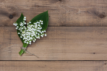 A bouquet of lilies of the valley tied with twine on a wooden background.