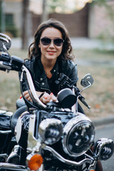 Fototapeta na wymiar Young beautiful biker woman in glasses and a leather jacket on a motorcycle. The concept of speed and freedom. Soft sective focus