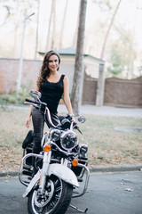 Fototapeta na wymiar Young beautiful biker woman in a black tank top and leather pants on a motorcycle. The concept of speed and freedom. Soft selective focus.