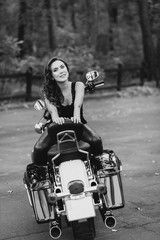 Young beautiful biker woman in a black tank top and leather pants sits on a motorcycle from behind. The concept of speed and freedom. Soft selective focus. Black and white photo.