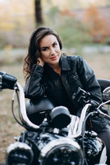 Fototapeta na wymiar Young beautiful biker woman in a black leather jacket on a motorcycle with a helmet in his hands. The concept of speed and freedom. Soft selective focus.