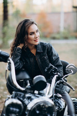Fototapeta na wymiar Young beautiful biker woman in a black leather jacket on a motorcycle with a helmet in his hands. The concept of speed and freedom. Soft selective focus.