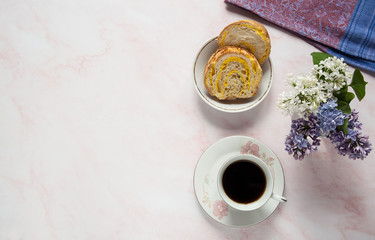 Spring composition. Cup of coffee, lilac flowers (Syringa vulgaris) and a sweet homemade turmeric bun on a pastel pink marble background. Free space. Top view.