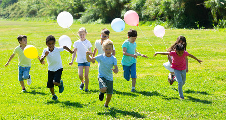 Obraz na płótnie Canvas Group of kids with balloons running in race and laughing in park