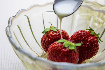 練乳をかけるガラスの器の中の苺