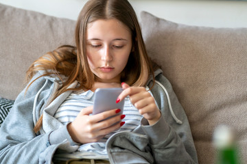 Bored teenage girl looking down at her mobile phone. Selective focus