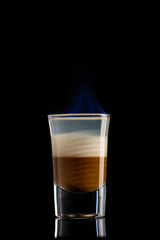 B52 coffee creamy alcohol cocktail in three layers in a shot glass on a black background