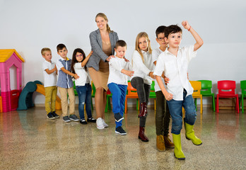 Obraz premium Positive female teacher playing circle game with children in classrom