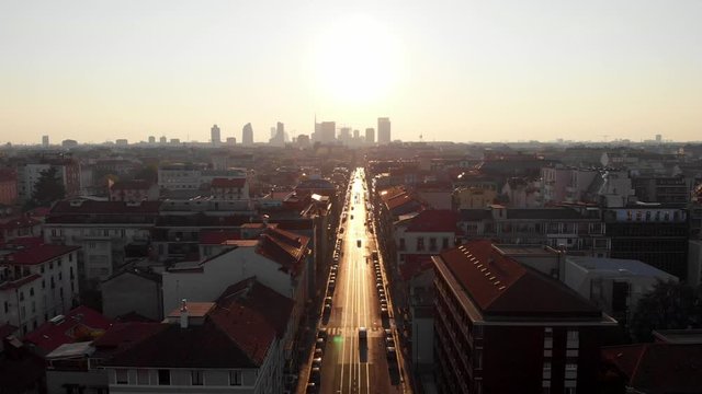 Drone aerial view of Milan skyline from above against bright sun over the city. Shot in Lambrate area during Coronavirus lockdown quarantine. Moving backward.