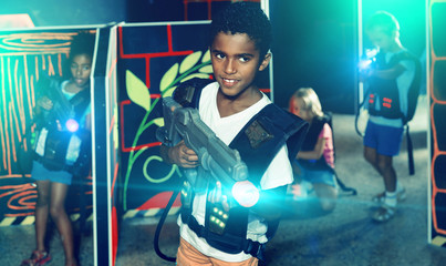Portrait of happy cheerful preteen boy with laser pistol posing in laser tag labyrinth