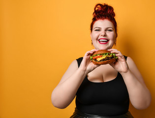 Happy smiling overweight plus-size woman going to eat bite burger cheeseburger she holds in hands...