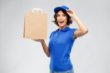 service and job concept - happy smiling delivery girl in blue uniform with takeaway food in paper bag over grey background