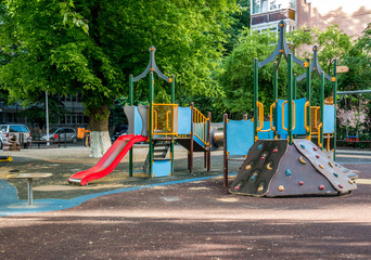 An empty children's playground in Bucharest, Romania. Children swings and slides in a park with green trees.