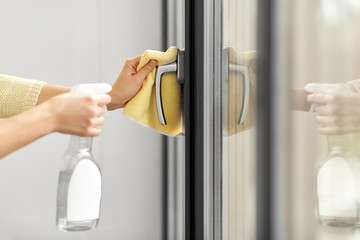 hygiene, health care and safety concept - close up of female hands cleaning window handle surface...
