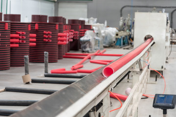 Factory for the production of plastic pipes.conveyor. The red pipe runs from one machine to another. Production process.