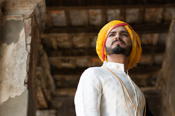 Low angle portrait of a young Indian man with ethnic wear with turban in an old vintage house. Indian lifestyle