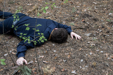 Murder in the woods. The body of a man in a blue shirt and trousers lies on the ground among the trees in the forest. Victim of an attack. .