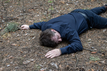 Murder in the woods. The body of a man in a blue shirt and trousers lies on the ground among the trees in the forest. Victim of an attack.
