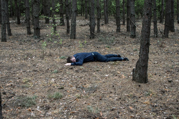 Murder in the woods. The body of a man in a blue shirt and trousers lies on the ground among the...