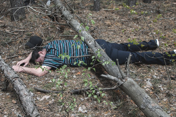 A body in the woods. A dead man in a blue t-shirt and trousers is pinned down by a fallen tree....