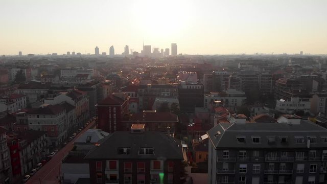 Drone aerial view of Milan skyline from above against bright sun over the city. Shot in Lambrate area during Coronavirus lockdown quarantine. Moving down and sideways and tilting up.