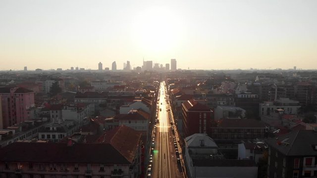 Drone aerial view of Milan skyline from above against bright sun over the city. Shot in Lambrate area during Coronavirus lockdown quarantine. Moving up and sideways over main street.