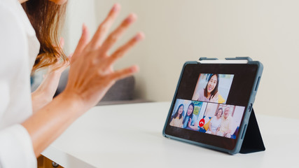 Young Asian business female using tablet video call talking with family while working from home at...