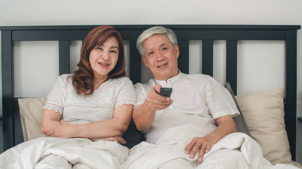 Asian elderly couple watching television in bedroom at home, Asia couple enjoy love moment while lying on the bed when relaxed at house. Enjoying time lifestyle senior family concept.