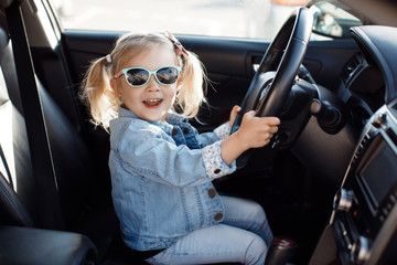 Cute little girl behind wheel of car.Baby girl sitting on the driver's seat in a family car.Child driving a passenger car. A little girl sits in the driver's seat in the car. - 350807872