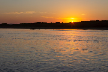 sunset over the river.  The sun is setting behind a small hill and reflecting off the water. 